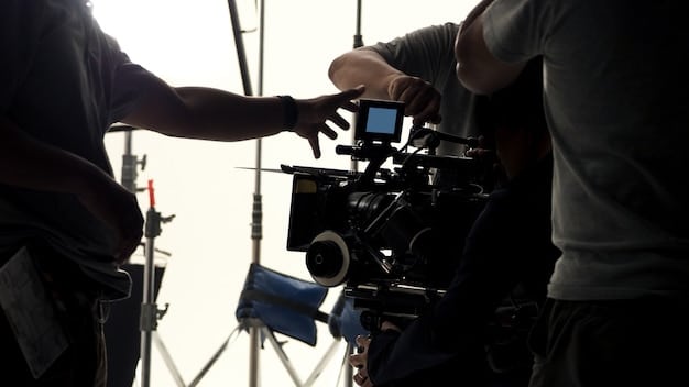 A close-up shot of a director's monitor displaying a film scene with actors, surrounded by camera equipment and crew members, emphasizing the collaborative and technical aspects of filmmaking.