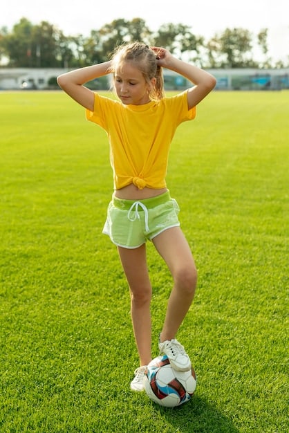A young girl, about 10 years old, actively playing soccer on a sunny field, dribbling the ball with focus and athleticism. Her uniform is bright, and the background shows other children in motion.