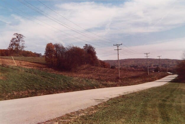 A rural road winding through farmlands with a new broadband installation truck working on power lines, symbolizing rural connectivity.